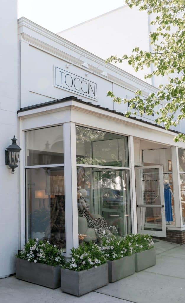 TOCCIN storefront on Main Street, Southampton, with hanging signage, window display, and planters of white flowers.