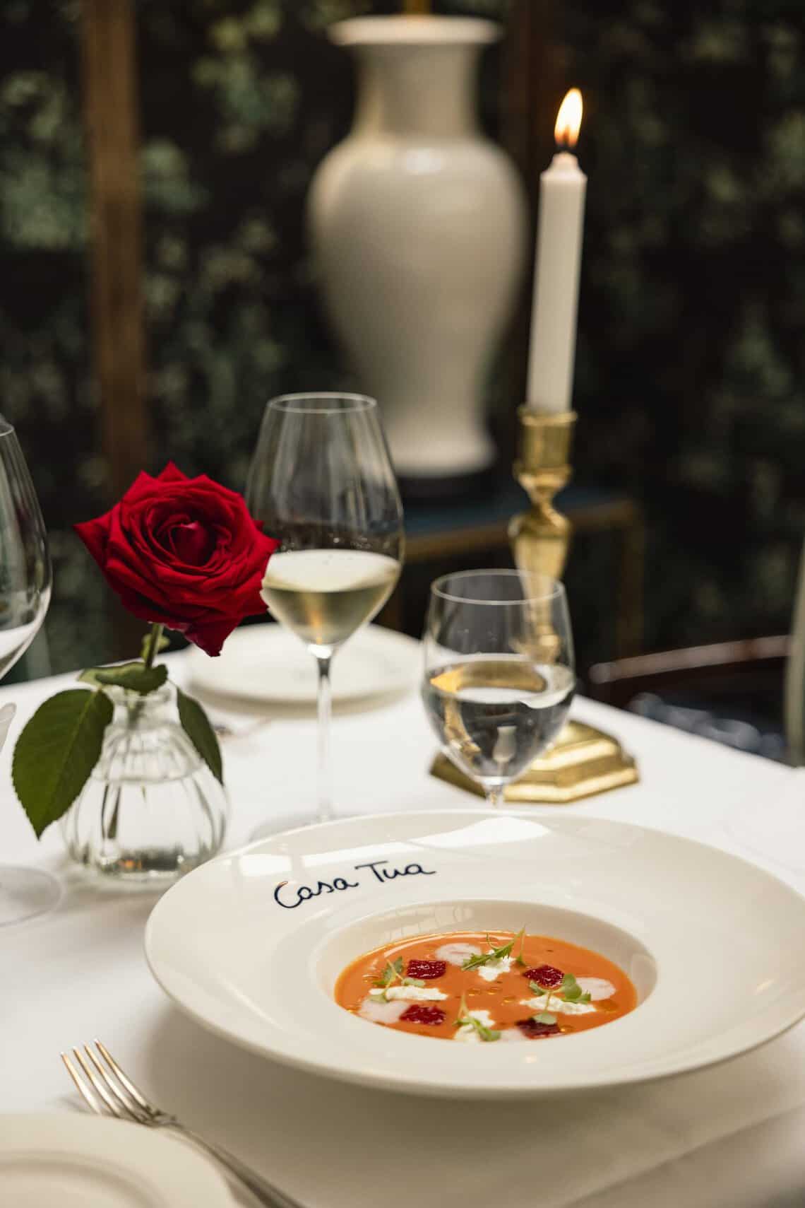 A table set with a white candlestick and a red rose at Casa Tua